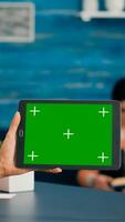 Back view of woman holding tablet computer with mock up green screen chroma key display. Caucasian female using touchscreen device for online browsing sitting in home office studio photo