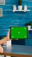 Woman looking at tablet computer with mock up green screen chroma key display browsing on internet searching lifestyle ideas. Freelancer using isolated device standing on desk office in living room photo