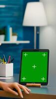 Freelancer woman holding cup of coffee looking at tablet computer with mock up green screen chroma key sitting on desk table. Caucasian female browsing on isolated device from home office room photo