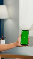 Social media woman holding touchscreen phone with mock up green screen chroma key sitting at modern office desk. Caucasian female working at online app using smartphone with isolated display photo