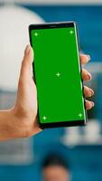 Hands of freelencer holding vertical mock up green screen chroma key smartphone. Business woman using isolated phone for browsing social networks sitting on office desk photo
