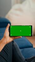 Close up of woman holding smartphone with mock up green screen chroma key display while sitting on sofa in living room. Freelancer using isolated touchscreen device for social networks browsing photo