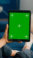 Caucasian female lying on sofa having online meeting on tablet computer with mock up green screen chroma key display. Woman using isolated touchscreen device for social networks browsing photo