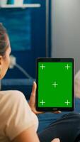 Business woman looking at tablet computer with mock up green screen chroma key display sitting on sofa in living room. Freelancer using isolated touchscreen device for social networks browsing photo