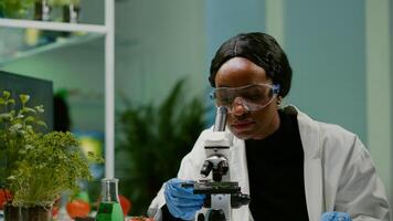 Portrait of scientist taking leaf sample with micropipette putting on slide under microscope for medical experiment. Chemist analyzing organic agriculture plants in microbiology scientific laboratory photo
