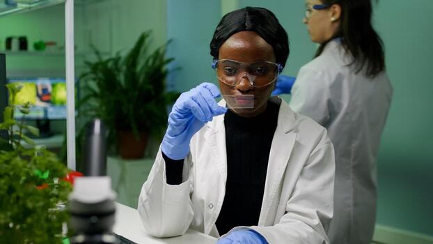 Botanist researcher scientist analyzing green liquid sample under microscope for microbiology experiment. Chemist specialist discovering organic gmo plants while working in pharmaceutical laboratory photo