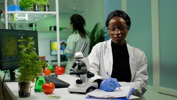Biologist researcher scientist looking at leaf sample under medical microscope while writing biological expertise on notepad. Chemist examining biological discovery working in microbiology lab photo