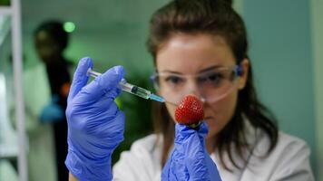 Closeup of biochemist researcher injecting healthy strawberry with dna liquid using medical syringe checking genetic test . Scientist biologist examining fruits in microbiology farming laboratory photo