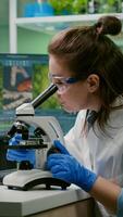 Portrait of biologist scientist in white coat working in expertise laboratory looking into microscope analyzing organic gmo leaf. Specialist researcher doing biochemistry experiment photo