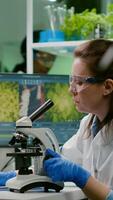 Pharmaceutical scientist looking at green leaf sample on microscope while writing genetic test on notepad. Biologist specialist analyzing organic gmo plants while working in microbiology food laboratory photo