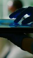 Chemist scientist woman checking dna sample test using tablet while her collegue typing microbiology experiment on computer in background. Medical team working in microbiology laboratory photo