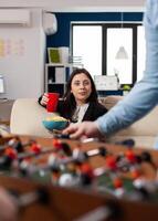 Caucasian woman holding cup of beer and chips after work looking at foosball table soccer game football for fun enjoyment entertainment. Happy worker drinking alcohol at party photo