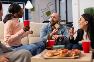 DIverse team of coworkers playing charades after work at office space. Multi ethnic friends enjoy guessing game of imiation as fun cheerful activity entertainment with food and drinks photo
