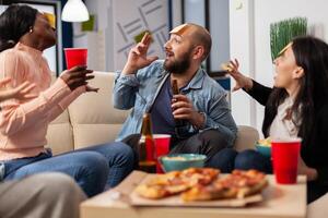DIverse team of coworkers playing charades after work at office space. Multi ethnic friends enjoy guessing game of imiation as fun cheerful activity entertainment with food and drinks photo
