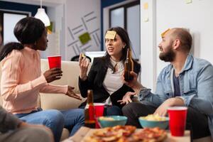 Cheerful group of colleagues enjoying a game of charades after work at office. Multi ethnic people play imitation concept for fun activity entertainment while eating pizza and drinking beer photo