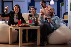 Colleagues with diverse ethnicity enjoy togetherness at office after work playing console game on tv. Multi ethnic workers having fun entertainment at indoors celebration party photo