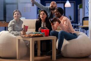 Happy people enjoying game on console after work at office while using controller joystick. Multi ethnic group of workers play for fun entertainment at party celebration indoors photo