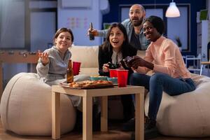 Happy people enjoying game on console after work at office while using controller joystick. Multi ethnic group of workers play for fun entertainment at party celebration indoors photo