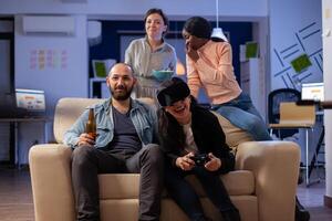 Group of workers playing game with vr glasses at office while using controller joystick. Diverse team enjoy bonding friendship togetherness at celebration party for enjoyment entertainment photo
