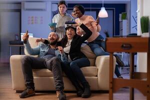 Team of multi ethnic coworkers using vr glasses after work for party at office. Group of diverse people enjoy gaming on console with controller joystick while having fun at celebration photo