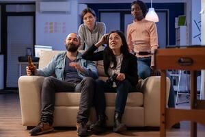 Group of diverse colleagues losing game with vr glasses on console tv while using joystick controller. Multi ethnic team having fun entertainment enjoyment at happy indoors celebration photo