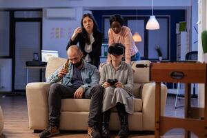 Diverse team of people use vr glasses on tv console at office party celebration after work. Multi ethnic colleagues play with joystick controller having fun enjoyment entertainment photo