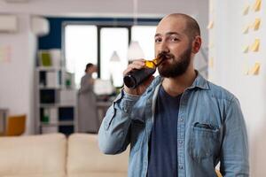 Portrait of business man drinking alcoholic beer from bottle, enjoying celebration with drinks after work hours. Happy worker meeting with colleagues in office to have fun with alcohol and snacks. photo