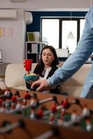 Portrait of young woman holding glass of beer at after work celebration, looking at foosball game play. Cheerful person enjoying drinks part after hours, celebrating with office workmates. photo