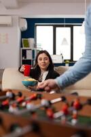 Portrait of business woman with beer bottle and chips snack celebrating after work hours in office. Happy adult having fun with drinks and foosball game play on table, enjoying leisure activity. photo