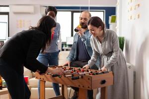 Office workmates playing foosball table game together after hours, enjoying alcoholic drinks and pizza. Man and women doing party celebration and having fun with match after work. photo