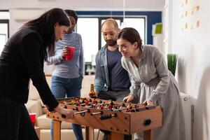 Businesspeople enjoying foosball game competition in office, celebrating with drinks and snacks after work hours. Group of friends having fun with soccer match table and alcohol. photo