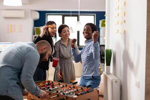 Happy woman celebrating foosball game win at office party after hours, enjoying alcoholic drinks with colleagues after work. Businesspeople having fun with leisure activity game. photo