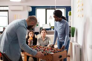 Man and african american woman playing foosball match game, having drinks in office after work. Office colleagues celebrating party with alcohol and pizza, enjoying after hours activity. photo