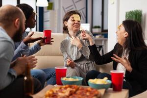 Diverse group of coworkers playing guess who game with sticky notes on forehead, enjoying fun activity with charades play. People guessing pantomime at drinks celebration after work hours. photo