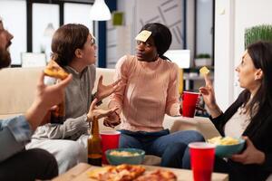 Multiethnic group of people play guessing game with sticky notes, laughing and having fun with drinks after hours. Office colleagues playing charades at party celebration with alcohol. photo