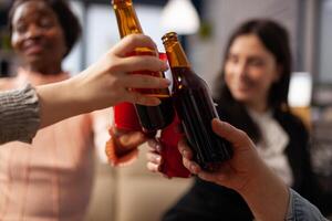 Office colleagues making toast and clinking glasses of alcohol, having drinks after work hours. Cheerful people enjoying champagne, wine or beer, doing cheers symbol at party. Close up. photo
