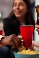 Cheerful people enjoying office party celebration with drinks and snacks after work hours. Coworkers eating chips from bowl, holding glasses and bottles of beer, doing fun activity. Close up. photo