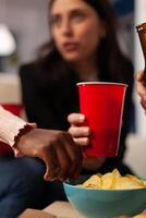 Office workers having fun with alcoholic beverage and chips at after work celebration. Colleagues enjoying beer in bottles and glasses, eating snacks and laughing together after hours. Close up. photo