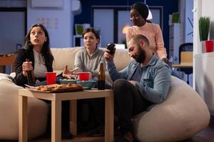 Sad man losing games play online with controller on tv console at office party, attending drinks celebration after work. Colleagues doing leisure activity with beer, pizza, snacks and game. photo