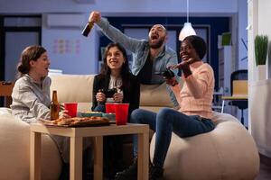 Happy workmates celebrating games win with drinks in business office after hours. Colleagues having fun with online game play, enjoying food and alcoholic beverage at celebration. photo
