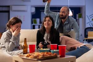 Sad woman losing games play on tv console with controller, attending office party after work hours. Colleagues using online game play at drinks celebration with food snacks. photo