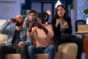 African american woman using vr glasses and playing games at office party with drinks after work hours. Colleagues having fun with virtual reality headset at celebration. photo