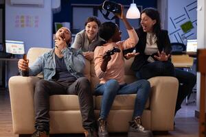 Happy colleagues using vr glasses on games play with controller, having fun with drinks after work hours. Business people enjoying leisure activity with virtual reality goggles at office party. photo