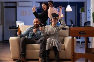 Happy woman celebrating games win on console, playing on tv with joystick and vr goggles. Cheerful people having fun with technology and devices at after work drinks celebration. photo