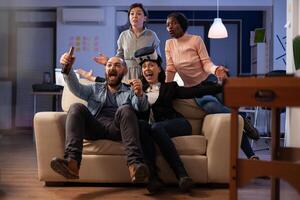Cheerful colleagues winning games play with vr glasses, using joystick on tv console and having fun. Office workmates enjoying party with alcoholic drinks and snacks after work. photo