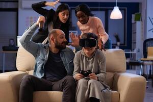 Multiethnic group of colleagues playing games with vr glasses at office party after work hours. Sad woman losing at gameplay on console with virtual reality headset and controller. photo