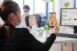 Back view of woman with face mask talking during business call keeping social distancing at workplace, safety precaution against infection with covid19 flu at workplace. photo