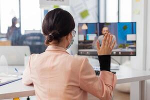 Woman discussing job project with business man during remote call in new normal office in time of global pandemic with covid19, wearing face mask safety prevention against infection. photo