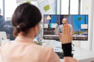 Woman greeting businessman during call from new normal business ofice, in time of covid19 outbreak. Coworkers discussing project on remote call wearing face mask as safety prevention. photo