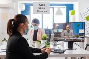 Coworkers discussing project during remote call from new workplace in time of global pandemic with coronavirus, wearing face mask as prevention to covid flu. photo